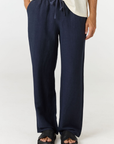 A person wearing dark navy wide-leg drawstring pants with a cream-colored top and black slide sandals, shown from the waist down against a plain light background.