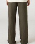 A person shown from the back wearing loose, wide-leg olive green pants and a light cream top against a plain light gray studio background.