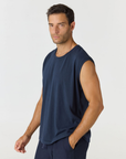 A man wearing a sleeveless navy blue muscle tank top and matching navy pants, standing against a light gray studio background.