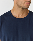 Close-up of a man wearing a dark navy blue crew-neck t-shirt against a light gray background.