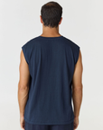 A man viewed from the back wearing a sleeveless navy blue shirt and matching navy pants against a light gray studio background.