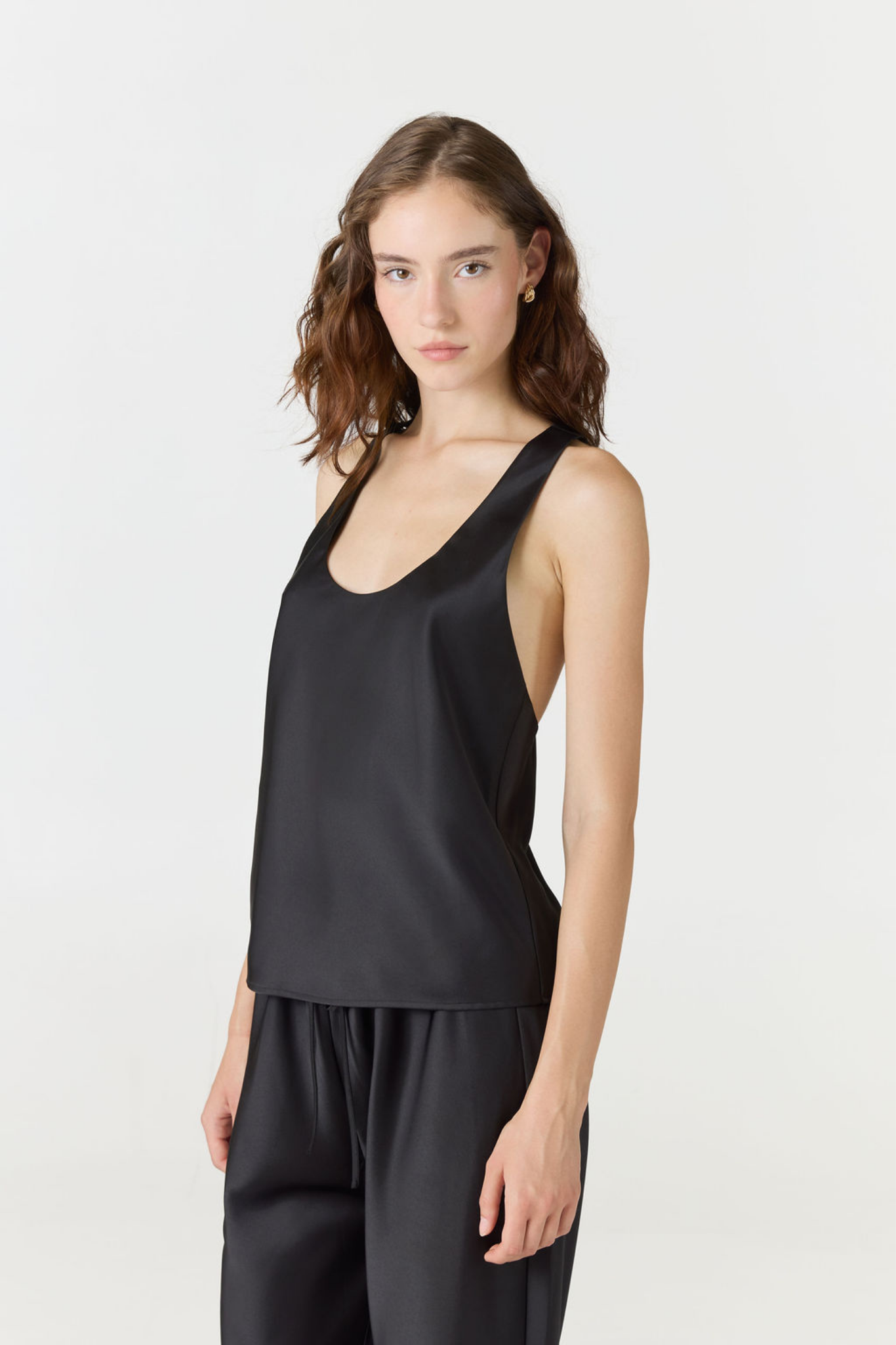 A woman modeling a black sleeveless satin-like top and matching black pants against a plain light gray studio background.