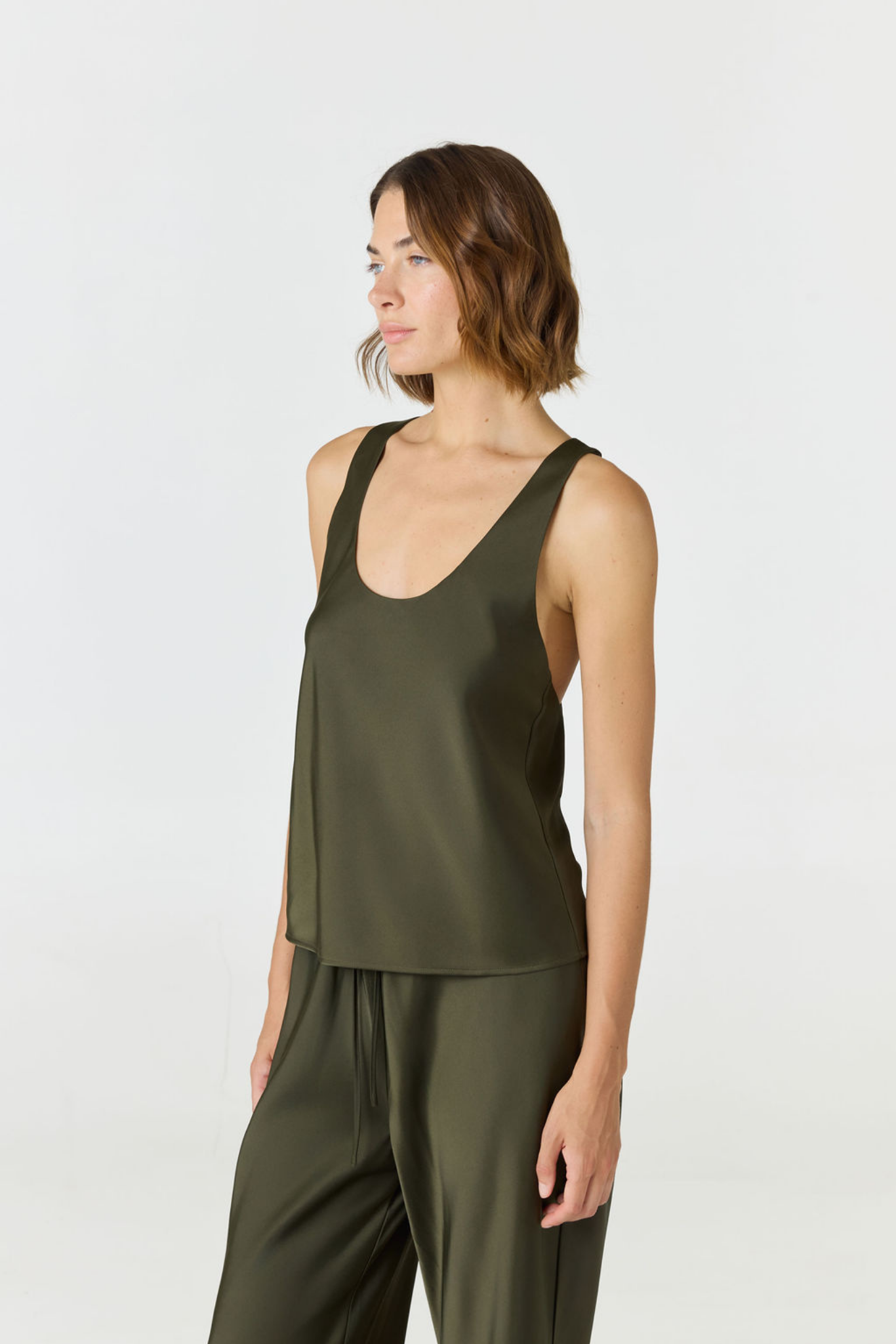 A woman modeling a sleeveless olive green top and matching wide-leg pants against a plain light gray studio background.
