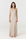 A woman modeling a sleeveless, floor-length maxi dress in a light beige or taupe color, standing against a plain white studio background.