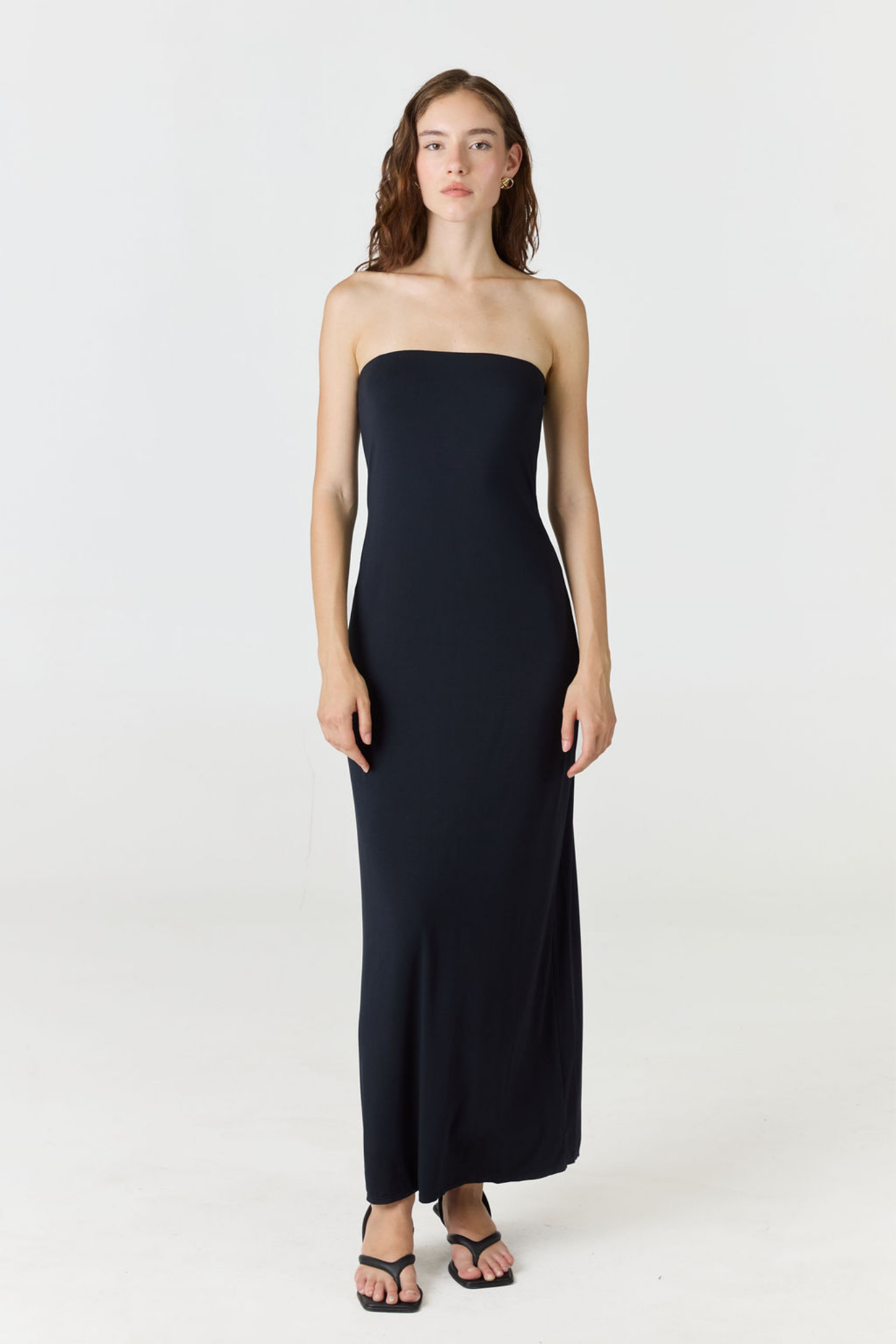 A woman modeling a strapless black maxi dress against a plain white studio background.