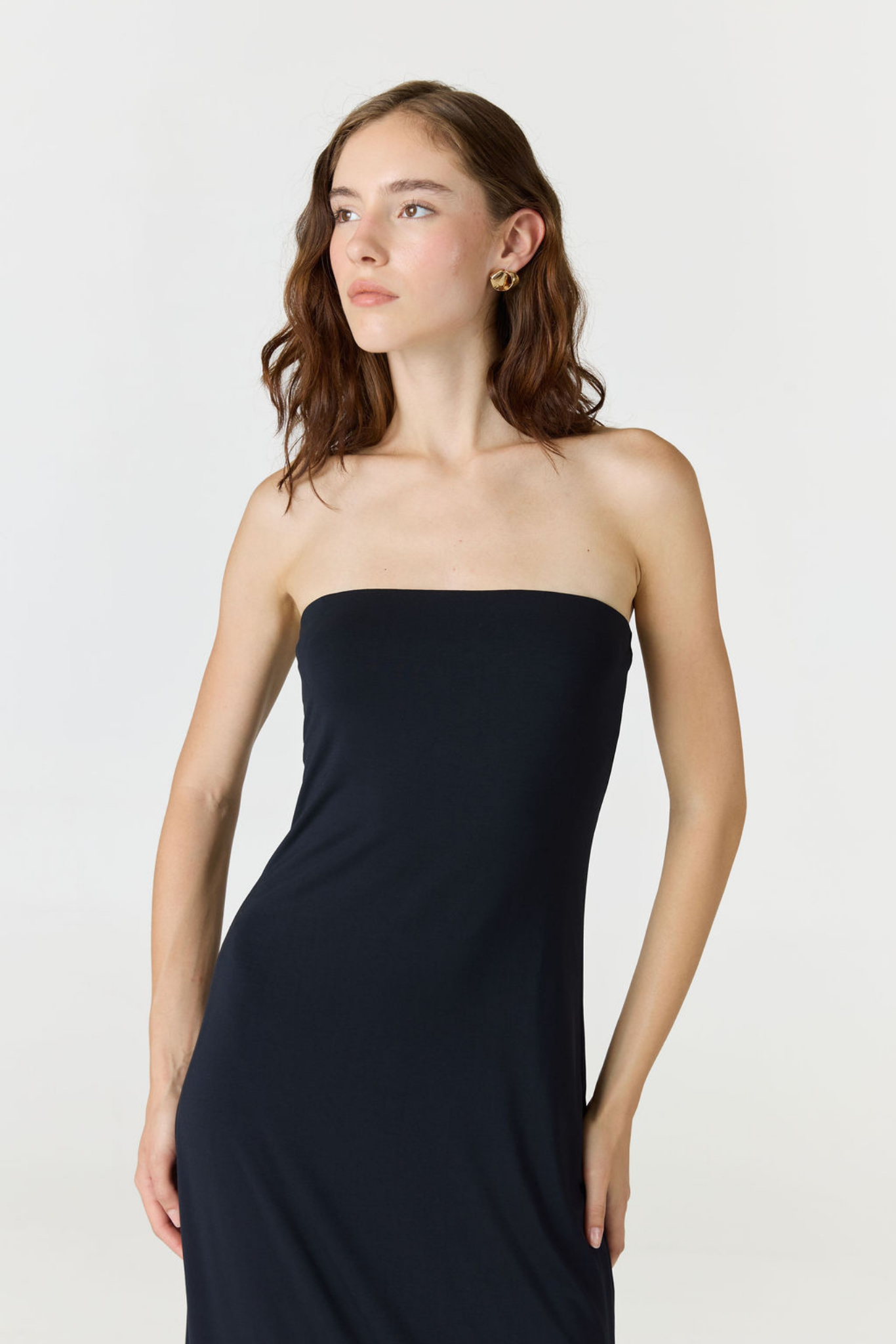 A woman modeling a strapless black tube dress against a plain light gray studio background.