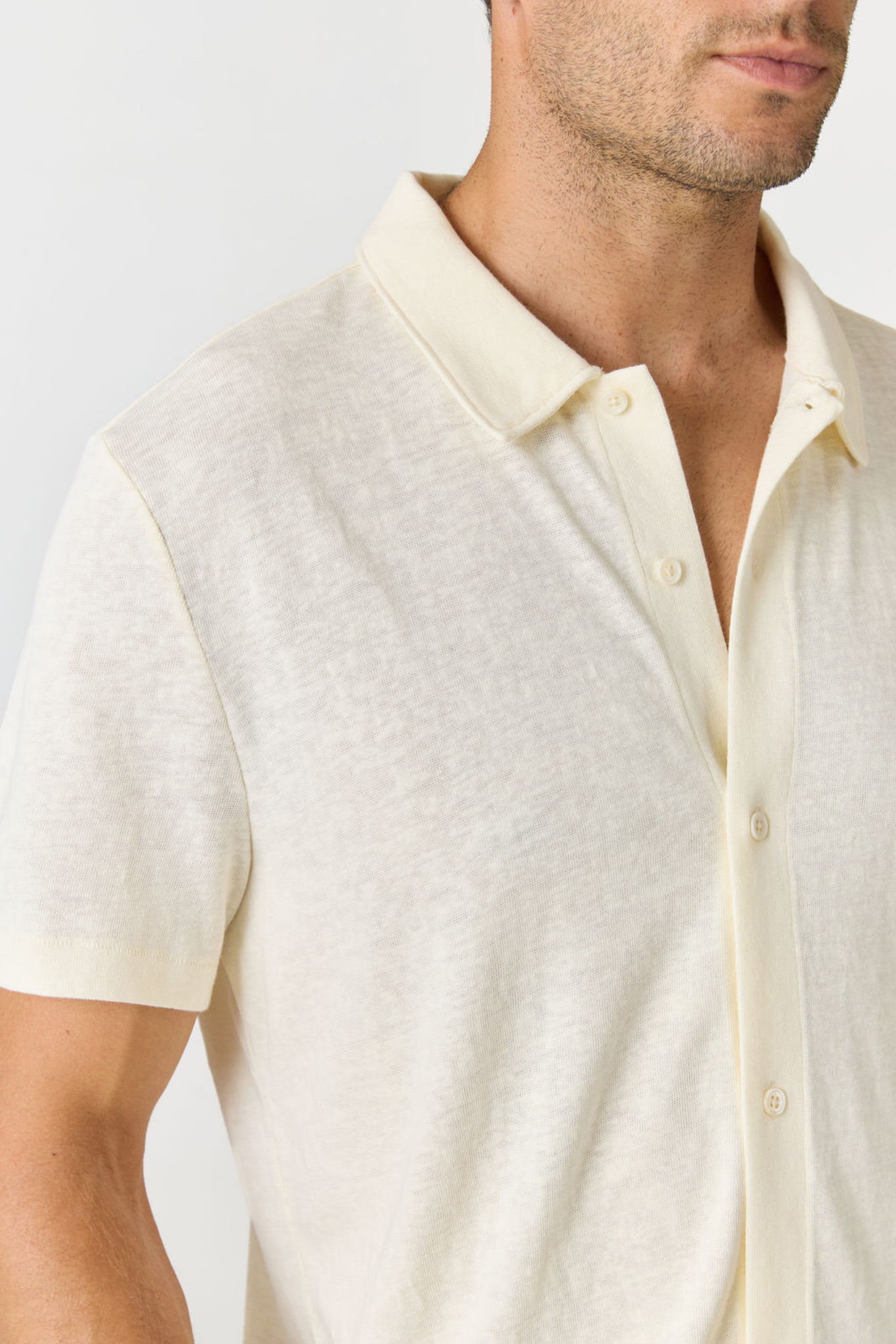 Close-up of a man wearing a short-sleeve polo shirt in a light cream or off-white color, showing the collar, buttons, and textured fabric.