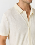 Close-up of a man wearing a short-sleeve polo shirt in a light cream or off-white color, showing the collar, buttons, and textured fabric.