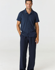 A man modeling a matching navy blue short-sleeve button-up shirt and wide-leg trousers set, standing against a plain light gray studio background.