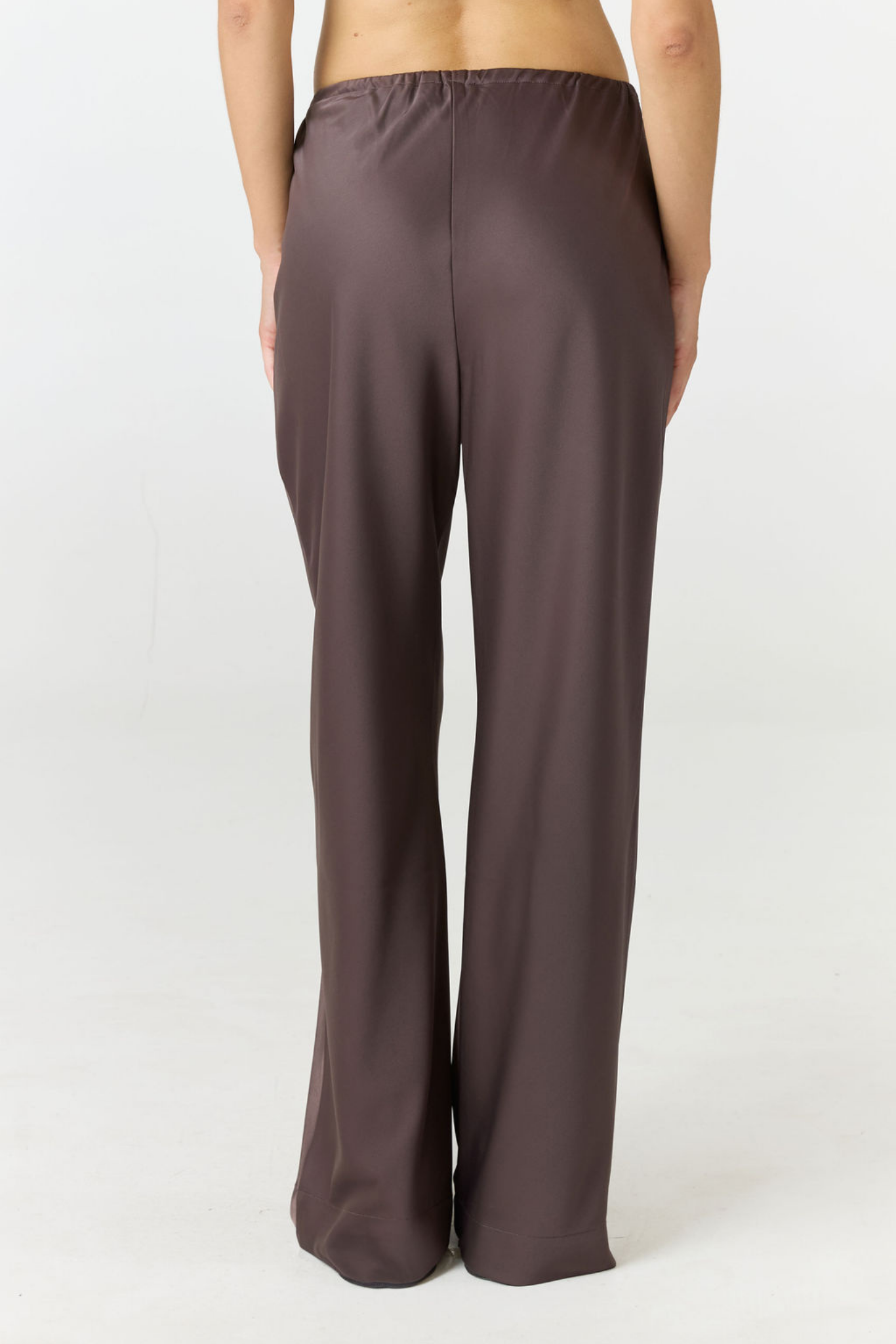 A person shown from the back wearing loose, wide-leg pants in a muted dark brown or taupe color, photographed against a plain light studio background.