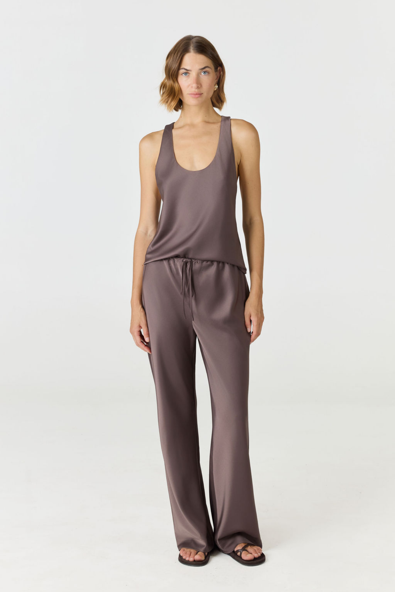 A woman modeling a matching two-piece loungewear set in a dusty mauve-brown color, featuring a sleeveless scoop-neck tank top and wide-leg pants, against a plain light gray studio background.