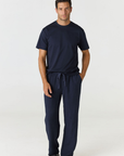 A man modeling a navy blue scrub set consisting of a short-sleeve crewneck shirt and matching drawstring pants, paired with black slide sandals, against a plain white studio background.