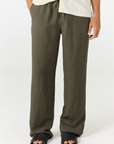 A person wearing loose, wide-leg olive green pants with a cream shirt and black sandals, shown from the waist down against a plain white studio background.