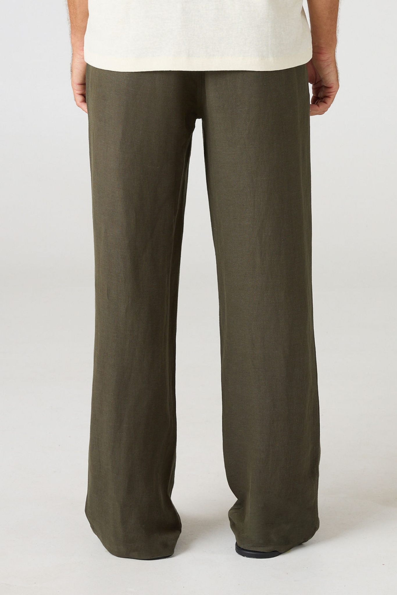 A person shown from the back wearing loose, wide-leg olive green pants and a light cream top against a plain light gray studio background.