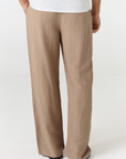 A person wearing loose, wide-leg taupe pants with a white top, shown from the back against a plain light gray studio background.