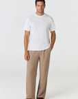 A man modeling a white short-sleeve crewneck t-shirt and beige wide-leg trousers, standing against a plain light gray studio background.