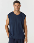 A man wearing a sleeveless navy blue t-shirt and matching navy pants, standing against a light gray studio background.