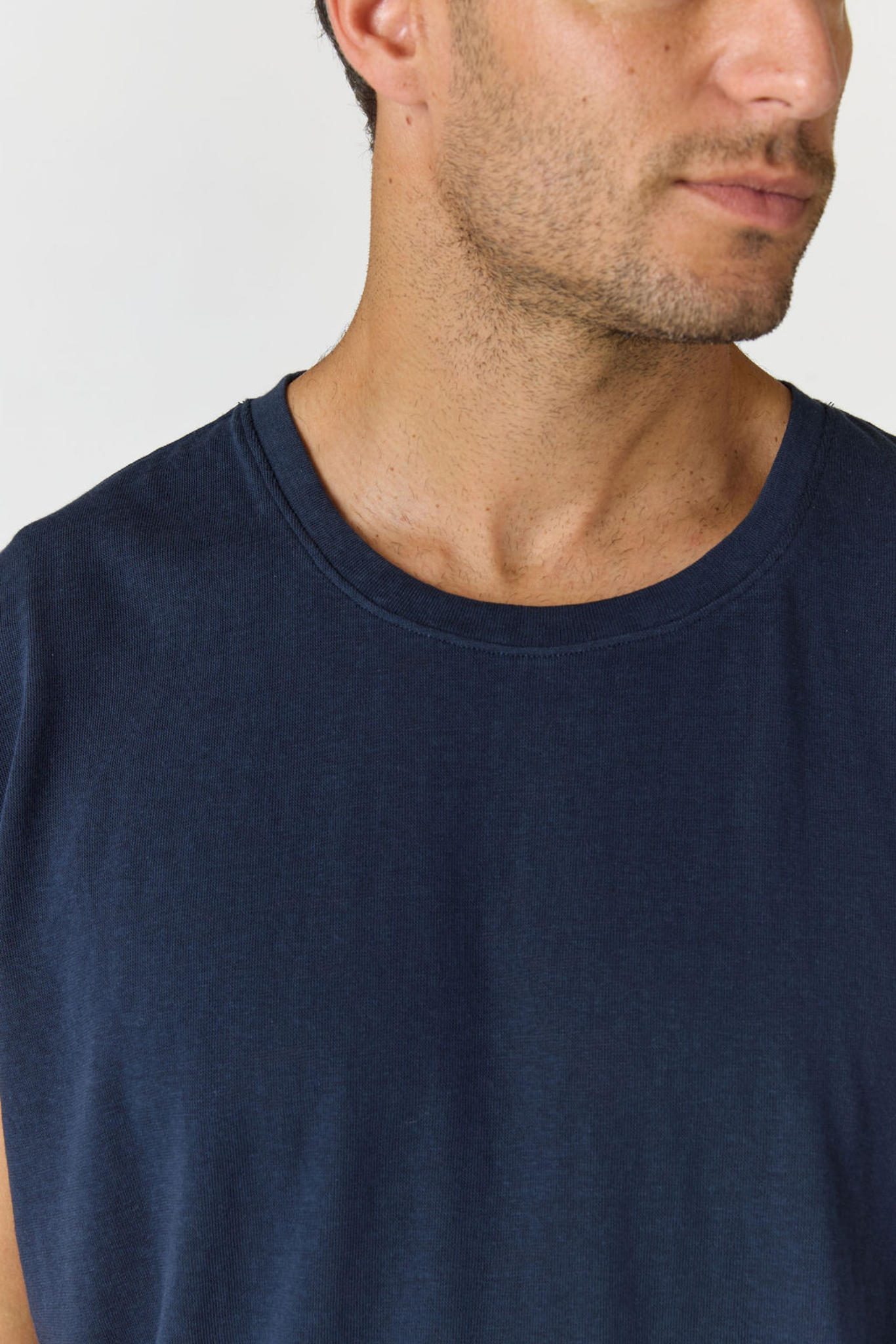 Close-up of a man wearing a dark navy blue crew-neck t-shirt against a light gray background.