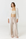 A woman modeling a light beige tube top, wide-leg satin pants, and a long white open-front cardigan over a white studio background.