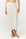 A woman wearing a white wrap sarong skirt with a side tie and thong sandals, shown from the waist down against a plain white studio background.